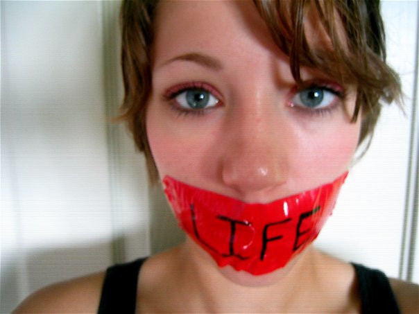 photo of the author in the past engaging in antichoice protest: has sticker over mouth that says "life" on it.